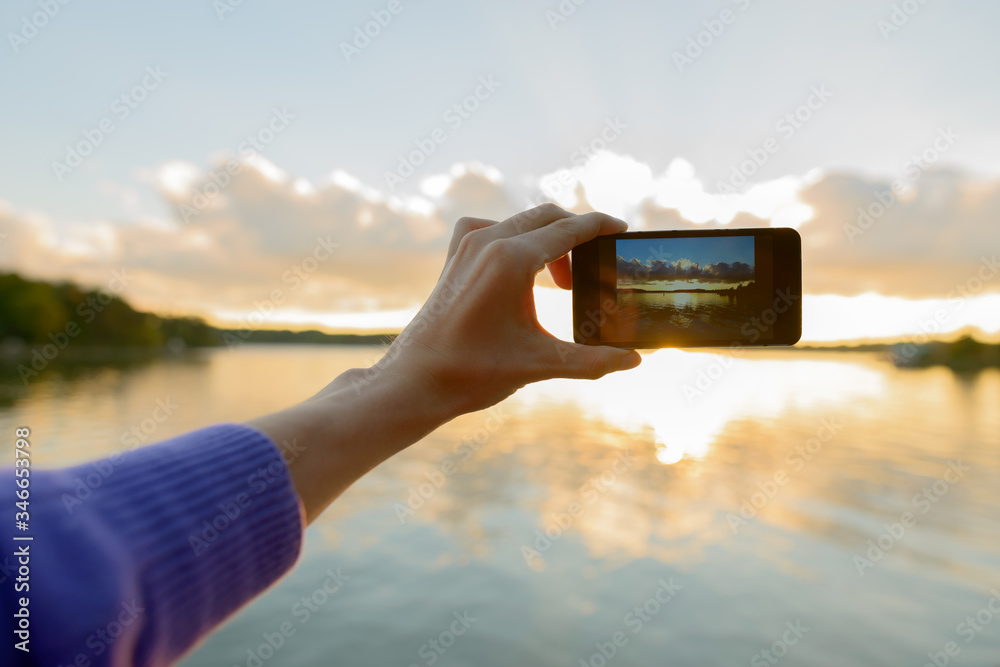 Fototapeta premium Hands of young man taking pictures with phone of beautiful sunset