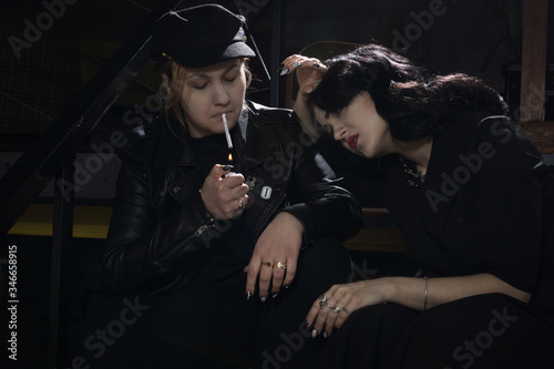 Gorgeous vintage 1950s lady and her friend sitting on the stairs in nightclub and smoke