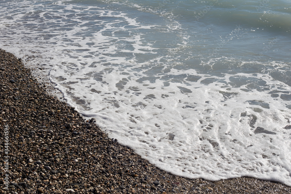 Stone pebbles, small round pebbles on the beach. Sea foam on the wolves. Stone pebbles, small round pebbles on the beach. Sea foam on the wolves.
