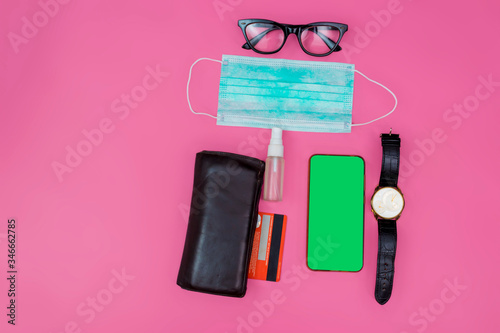 Mockup mobile phone with facial masks, wristwatch, credit card, wallet and Alcohol Mini Hand Sanitizer Spray on a pink workspace