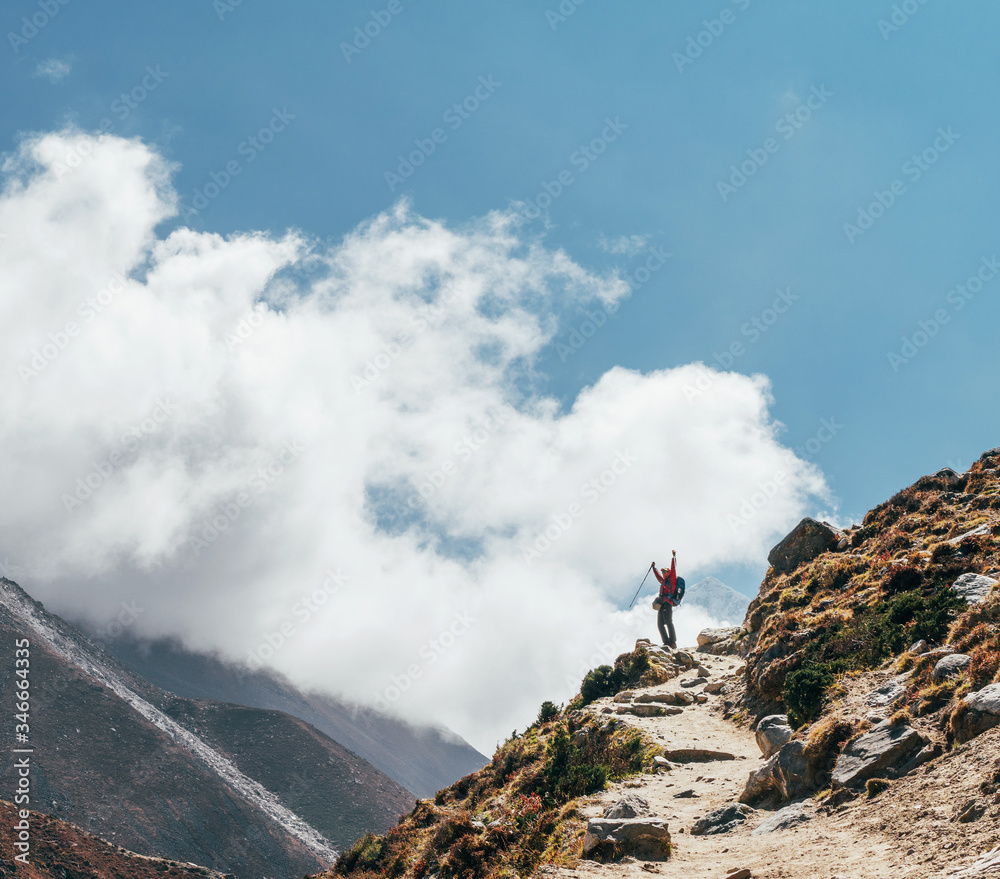 Young hiker backpacker female taking brake in hike walking during high altitude Everest Base Camp (EBC) route with snow Himalayan peaks on background.She using trekking poles. Active vacations concept