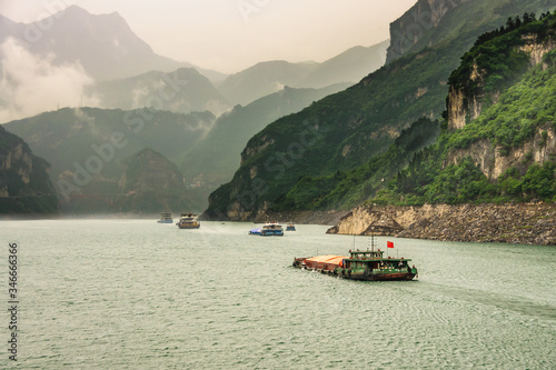 Zigui, China - May 6, 2010: Xiling gorge on Yangtze River. Landscape of Green mountain slopes along greenish water with multiple tarnsport barges sailing. Cloudscape descends on sides.