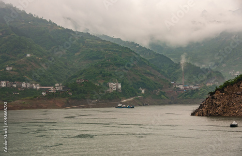 Xiangxicun, China - May 6, 2010: Xiling gorge on Yangtze River. Xiangxi river empties in Yangtze. with green mountains and gray descending cloudscape as backdrop. Smoke stack in distance. photo