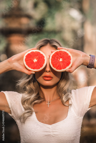 Beauty Model Girl takes a juicy grapefruit. Beautiful joyful young girl, funny blond hairstyle and pink make-up. Holding orange slices in the face