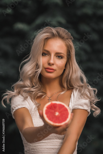 Woman with long blond hair girl colorful eyes makeup holding grapefruit citrus. Healthy diet food.