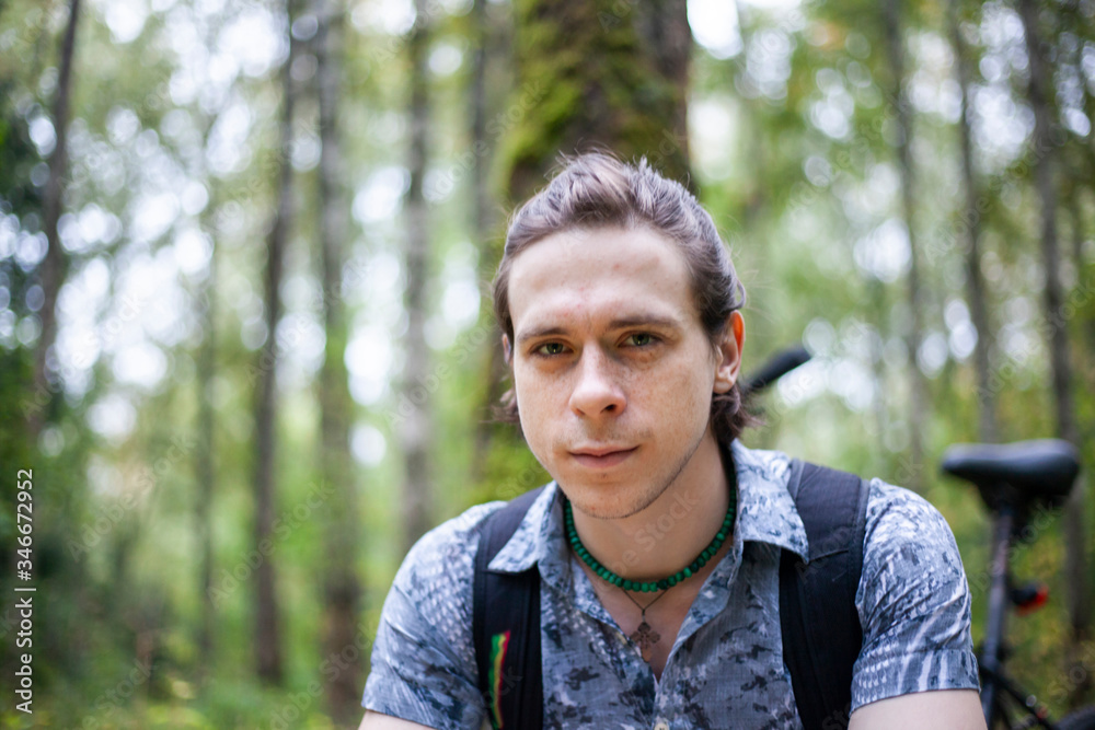 Portrait of a young man in a park. White guy with long hair. Summer portrait shot in nature. Man's face in natural light.