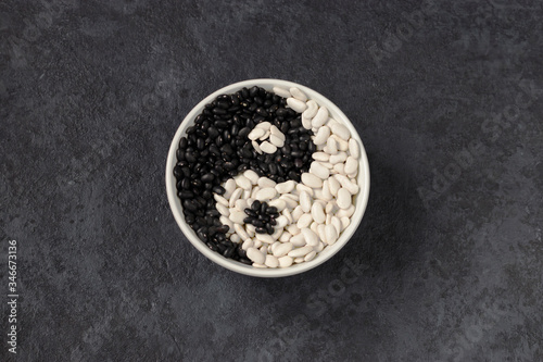 Beans on a dark background. White beans and black beans in a a gray plate. Sign yin yang. Horizontal position