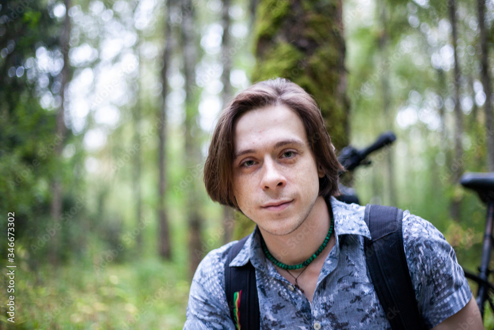 Portrait of a young man in a park. White guy with long hair. Summer portrait shot in nature. Man's face in natural light.