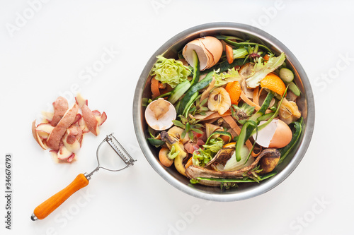 Organic food waste in iron bowl, potato peeling and knife on white table. Food leftovers ready to compost. Environmentally responsible behavior, ecological, recycling waste concept. Copy space.