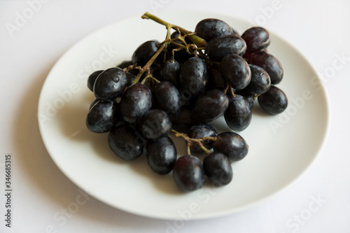A bunch of juicy black grapes on awhite plate.
