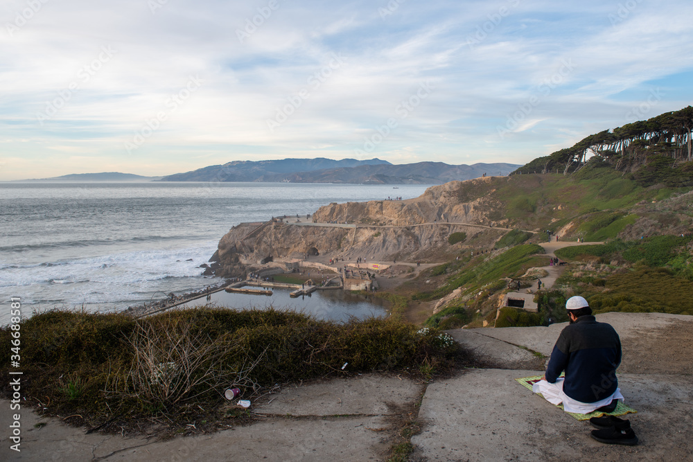 Fototapeta premium Man is praying on cliff at sunset ocean, San Francisco, California