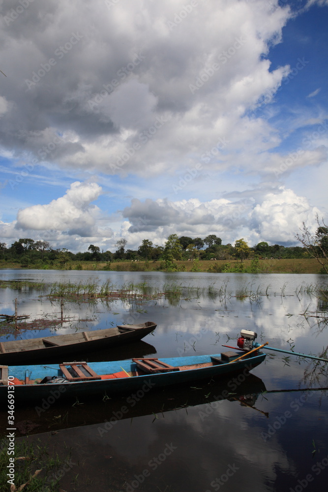 Landscape of Amazon rainforest with two floating boats on water under blue sky in Brazil