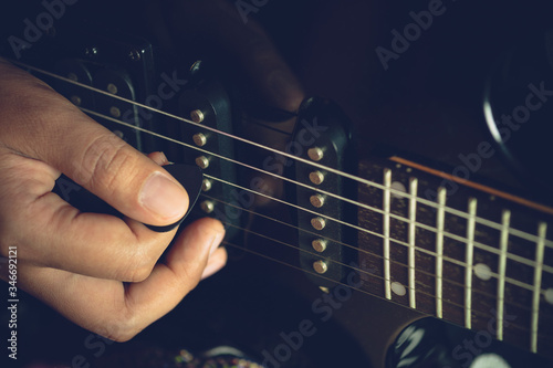 Guitarist is rehearsing playing black vintage electric guitars. Closeup girl's hand is holding the pick and putting it on guitar string in dark studio. Concept of musical instruments and rock music.