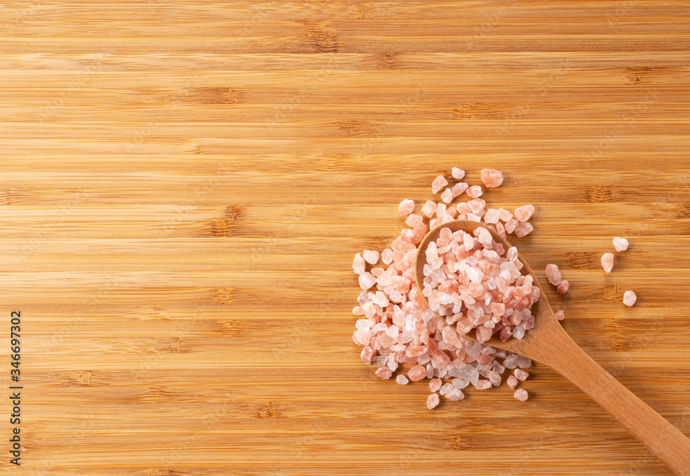 Wooden spoon with pink rock salt placed on wooden background