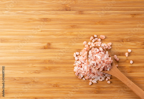 Wooden spoon with pink rock salt placed on wooden background