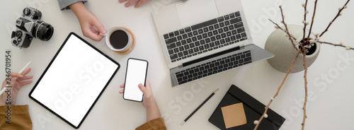 Overhead shot of two graphic designer working together with mock-up digital devices, camera and other supplies
