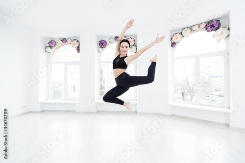 Young slim fitness woman in black sports clothing jumping high on window background