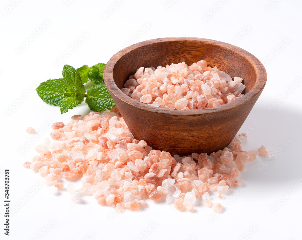 Pink rock salt in a wooden bowl with mint placed on a white background Pink rock salt in a wooden bowl with mint placed on a white background