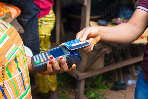 black lady shopping in a local market using credit card for payment. Young African trader holding a point of sale machine with a credit card. Woman making payment with Bank card