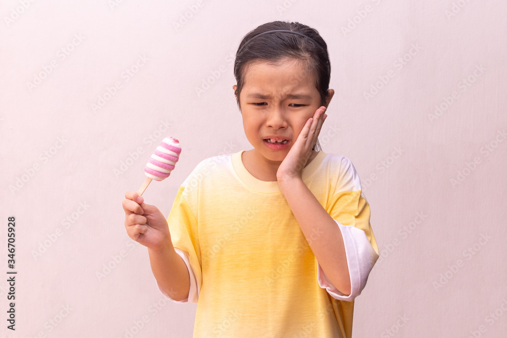 Asian girl with hypersensitive teeth eating eating a colorful frozen popsicle in the summer Asian girl with hypersensitive teeth eating eating a colorful frozen popsicle in the summer