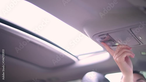 The girl presses the button to open the hatch in the car and the hatch opens, showing bright light from the sky. No face, close up photo