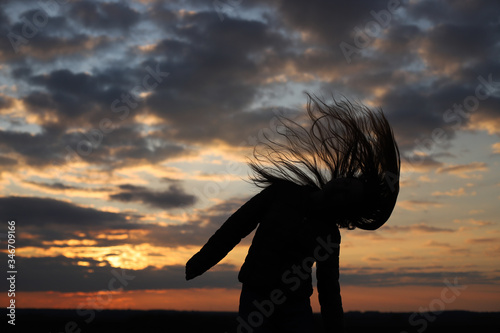 The silhouette of a young girl feels happy and shakes her head. The moment of sunset. Long hair loose. Shadow of a girl on a sunset background. © Ekaterina Ershova