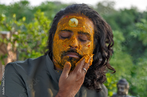 Face portrait of attractive bearded Indian man applying facial clay mask with turmeric and cucumbers