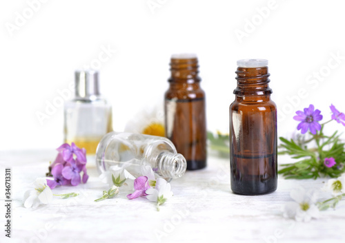 bottles of essential oil and colorful petals of flowers on white table