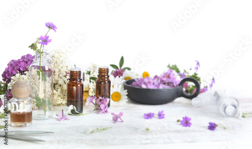 bottles of essential oil and colorful petals of freshness flowers on white table