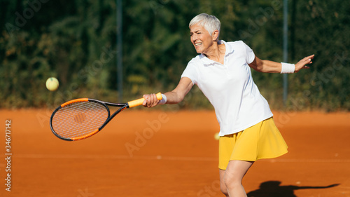 Smiling Elderly Woman Playing Tennis as a Recreational Activity © Microgen
