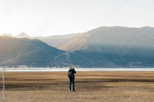 Hipster man traveler with sweater and backpack traveling at Napa Lake  Photographer taking photo to mountain view in trip Shangri-La Yunnan China. Explore  Adventure and Asia Solo travel concept