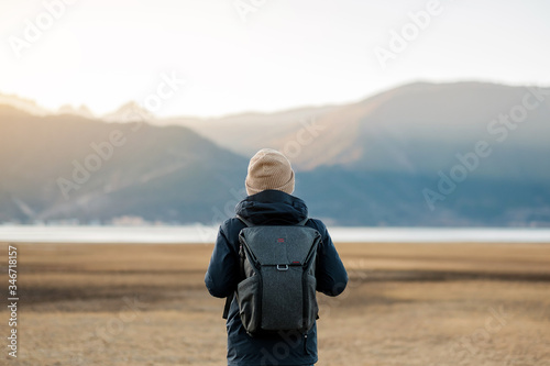 Fotografia Hipster man traveler with sweater and backpack traveling at Napa Lake, Happy young Hiker looking mountain and sunset in trip Shangri-La,Yunnan,China