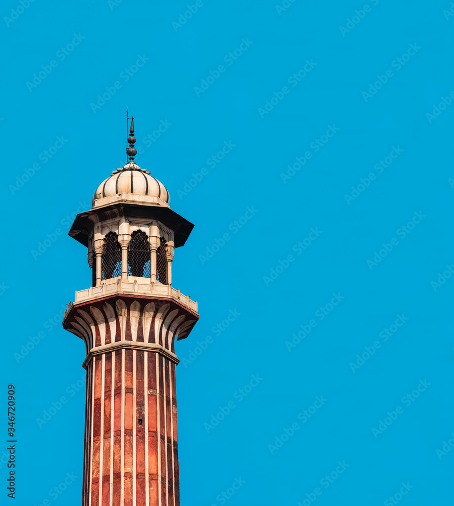 A single isolated Minaret of Jama masjid mosque in Delhi, India with clear blue sky background. As a graphic resource and background for Islamic culture and Eid festival with space for text.