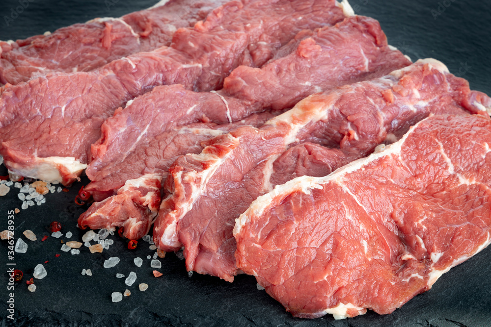 Fresh raw beef steaks on a black slate plate . Raw rib eye steaks on a slate plate with salt and pepper. Steaks with spices  on black slate stone board.