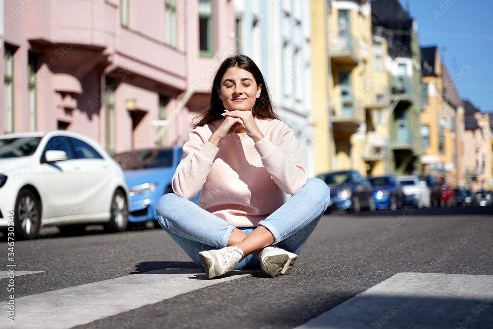 Young woman meditating in lotus position in front of modern city on road. Antistress concept