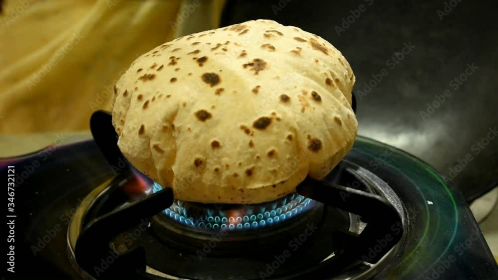 indian house woman making chapati bread on open flame by tongs, close up of chapati cooking on fire