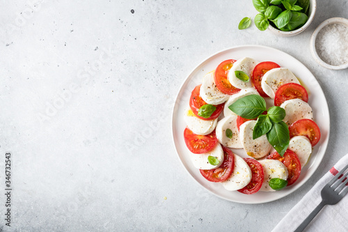 Italian caprese salad with sliced tomatoes, mozzarella, basil, olive oil on a light background. Top view, place for text. photo
