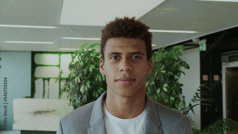 Fototapeta premium Young African-American man in elegant suit standing in modern office and smiling happily at camera.