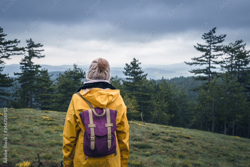 Woman in yellow raincoat and backpack hiking in nature