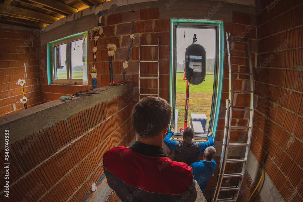 Two male workers installing a modern glass window into a new house ...