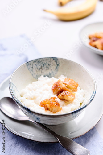 Creamy Rice Porridge or Pudding with caramelized bananas in bowl on grey concrete background. Selective focus