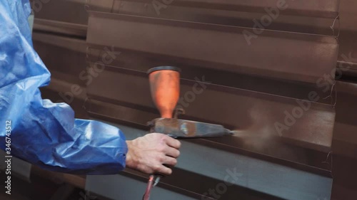 A professional paint gun in a person's hand sprays brown paint on a metal product