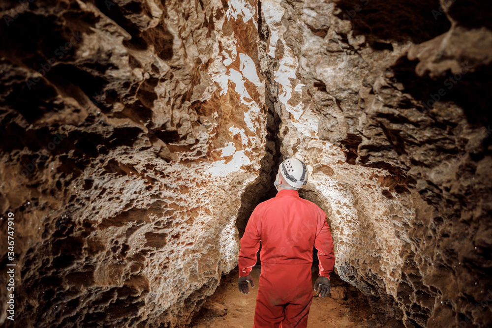 Man walking and exploring dark cave with light headlamp underground. Mysterious deep dark, explorer discovering mystery moody tunnel looking on rock wall inside.