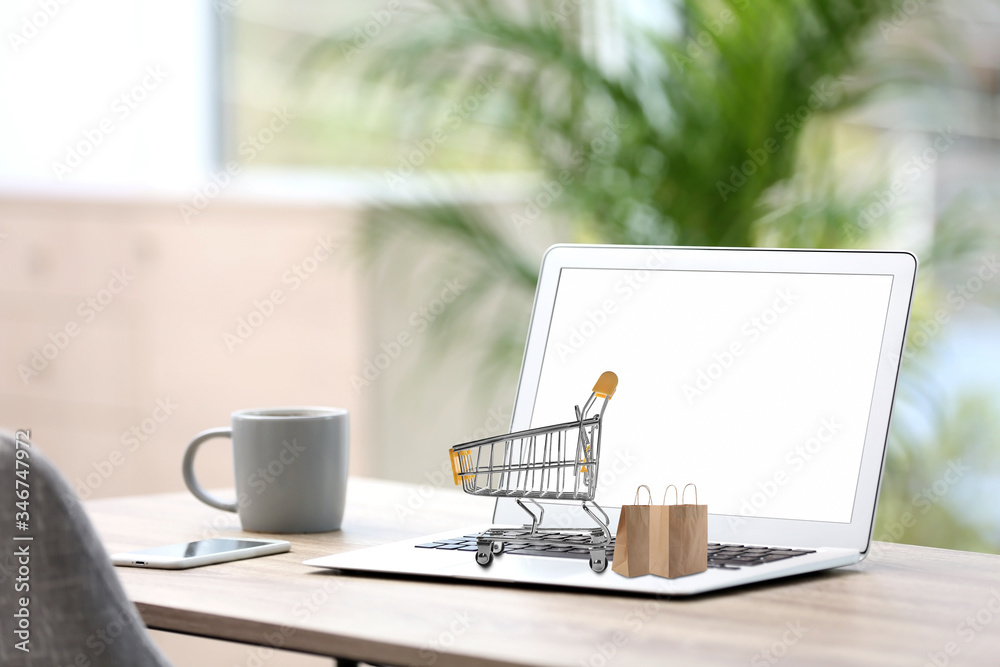 Online shopping. Modern laptop with small cart and bags on table