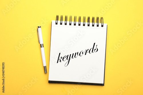 Stylish notebook with text KEYWORDS and pen on yellow background, top view
