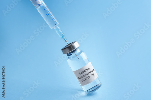 Filling syringe with coronavirus vaccine on light blue background