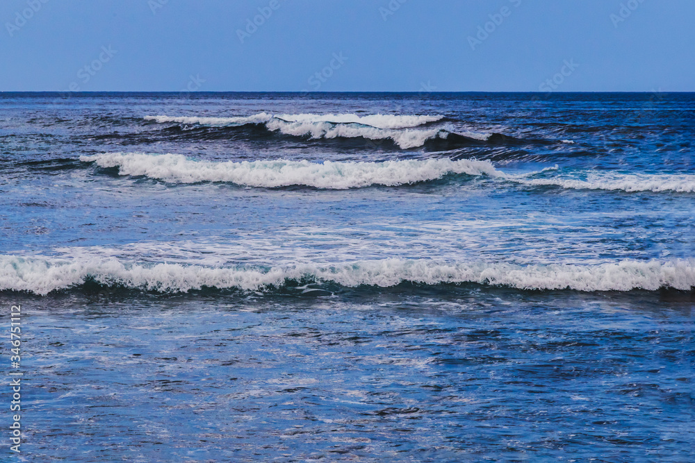 Calm blue sea on Nusa Cennigan island, near Bali, Indonesia. Multiple small waves gently moving towards shore. 
