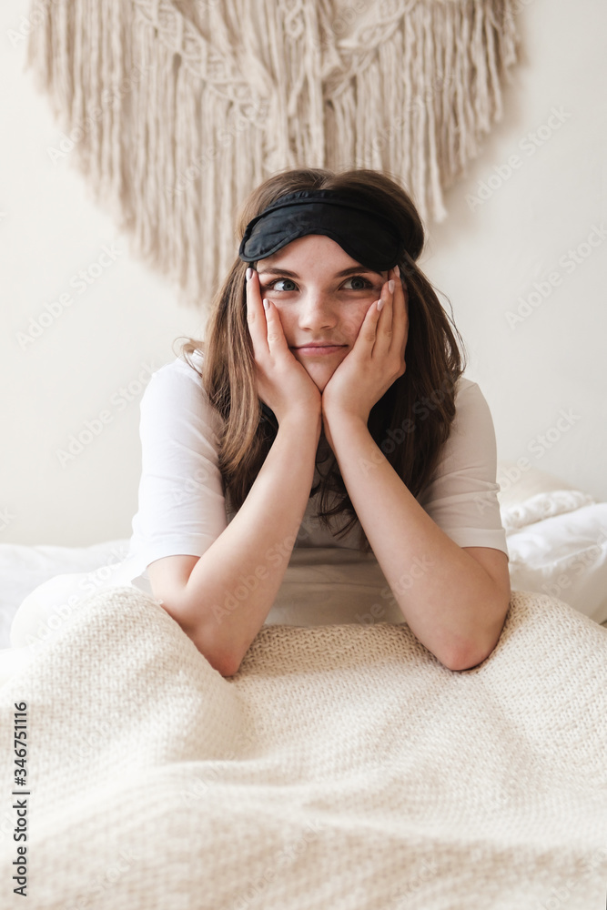 Young beautiful girl lying in comfortable bed and a mask for sleep in the morning at cozy home. Self-isolation, stay home during quarantine, pandemic. Young beautiful girl lying in comfortable bed and a mask for sleep in the morning at cozy home. Self-isolation, stay home during quarantine, pandemic.