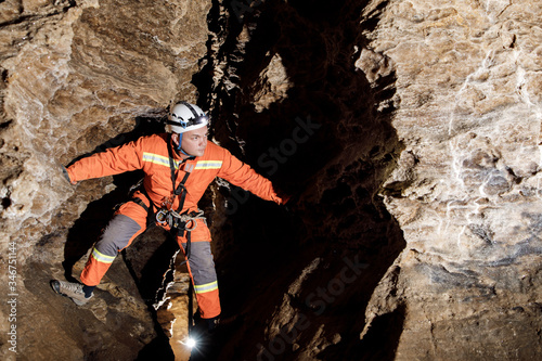 Speleologist descend by the rope in the deep vertical cave tunnel. Cave man hanging over abyss. View from the top og the tunnel. photo