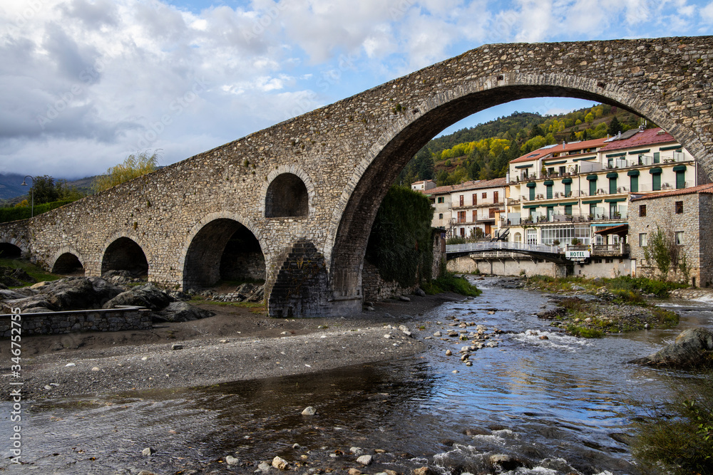 Old medieval bridge made of stones over a small river in a village close to the mountains in Europe.